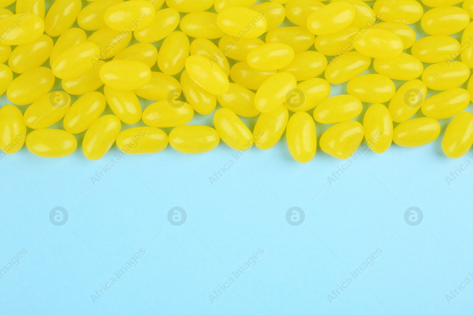 Photo of Many delicious lemon jelly beans on light blue background, flat lay. Space for text