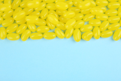 Photo of Many delicious lemon jelly beans on light blue background, flat lay. Space for text