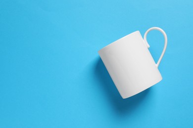 Photo of One white ceramic mug on light blue background, top view. Space for text
