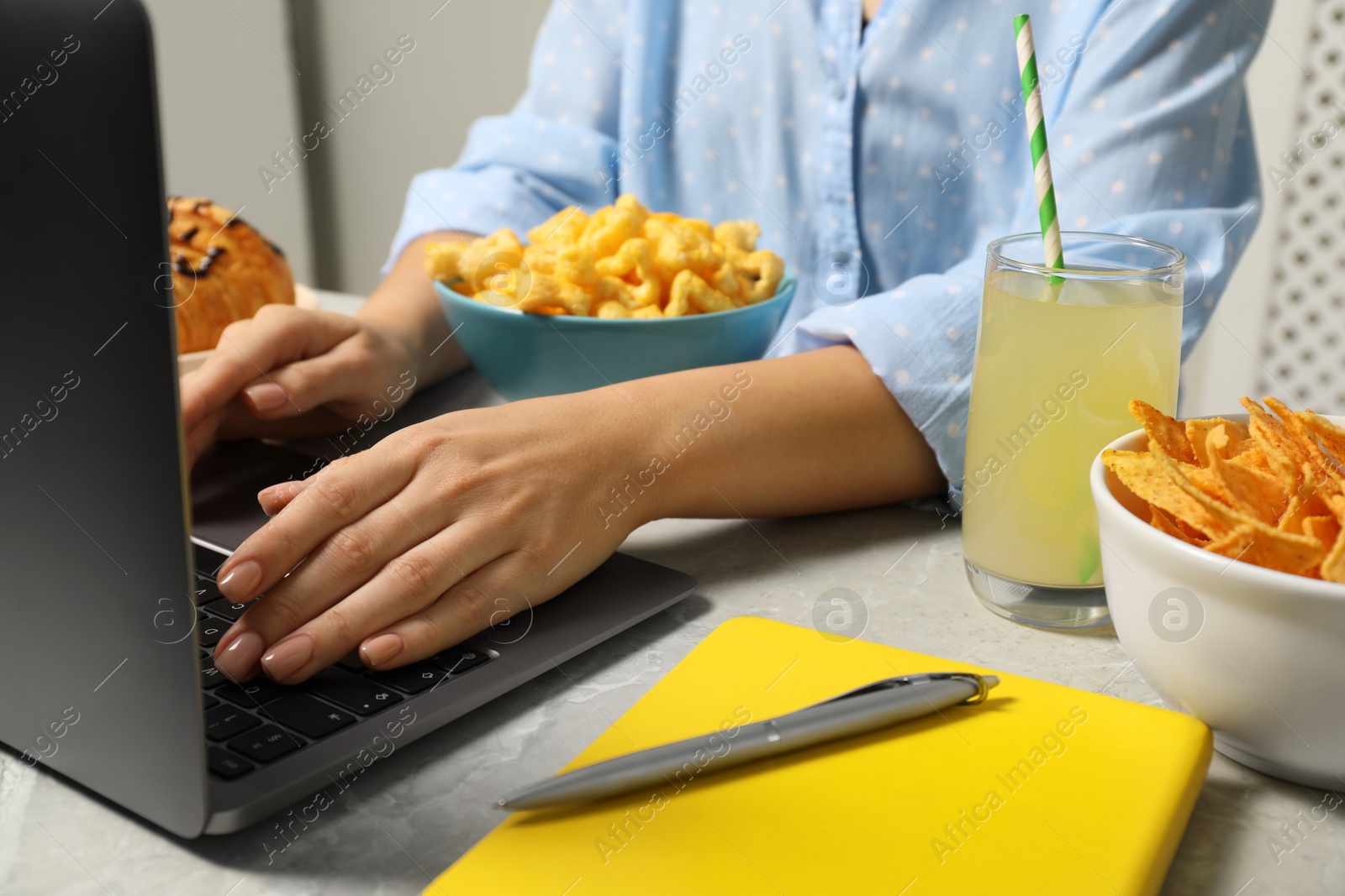 Photo of Bad eating habits. Woman using laptop surrounded by different snacks at light grey marble table, closeup