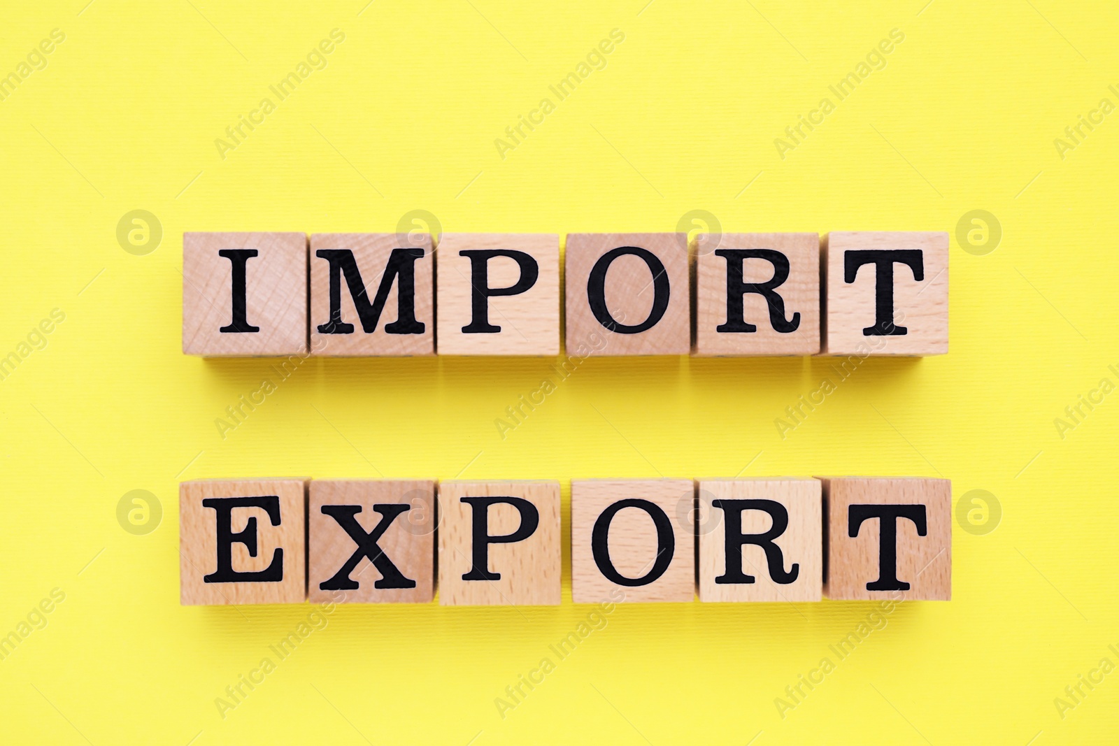 Photo of Words Import and Export made of wooden cubes with letters on yellow background, top view