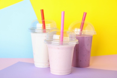 Photo of Different tasty milk shakes in plastic cups on color background