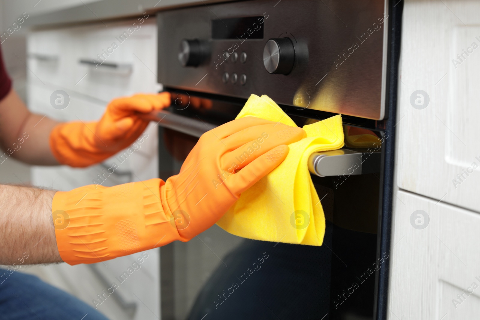 Photo of Young man cleaning oven with rag in kitchen, closeup