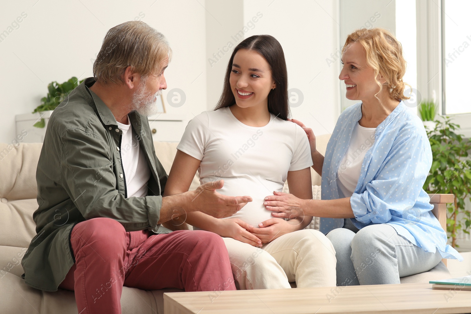 Photo of Happy pregnant woman spending time with her parents at home. Grandparents' reaction to future grandson