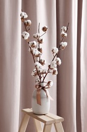 Photo of Vase with beautiful bouquet of white fluffy cotton flowers on wooden decor ladder