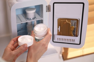 Photo of Woman taking cosmetic product from mini fridge indoors, closeup
