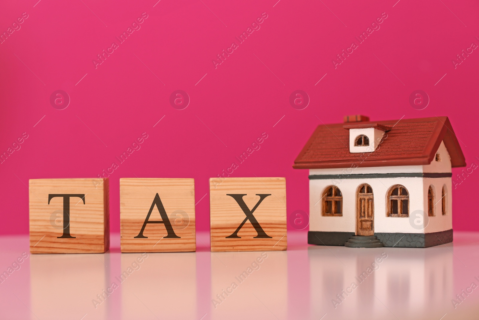Photo of Wooden cubes with word TAX and house model on table against color background