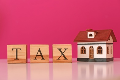 Wooden cubes with word TAX and house model on table against color background