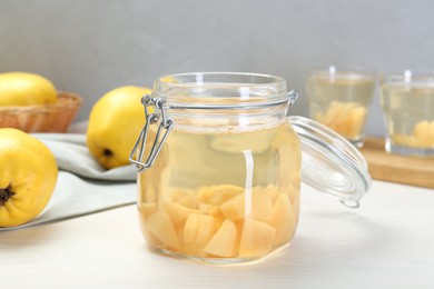 Delicious quince drink in glass jar and fresh fruits on white wooden table