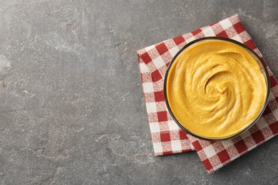 Photo of Tasty mustard sauce in bowl on grey textured table, top view. Space for text