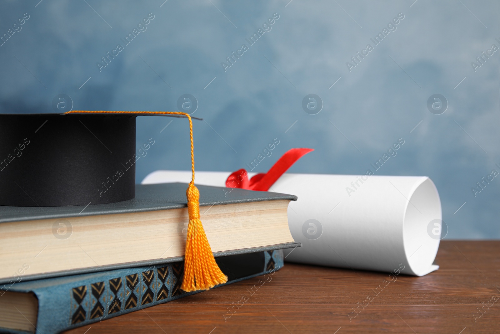 Photo of Graduation hat, books and student's diploma on wooden table against light blue background