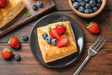 Photo of Fresh delicious puff pastry with sweet berries on wooden table, flat lay