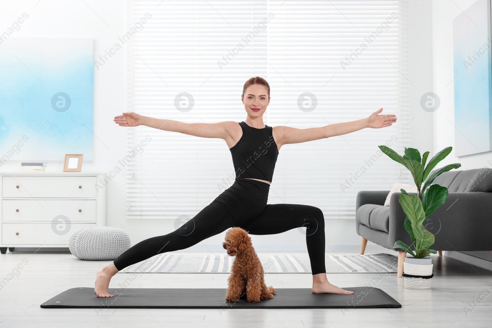 Photo of Young woman practicing yoga on mat with her cute dog at home