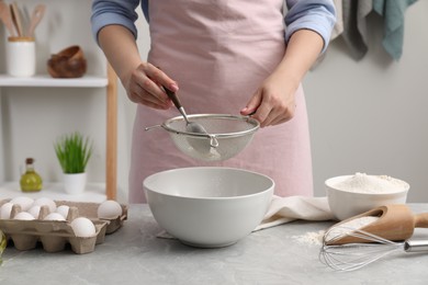 Photo of Making tasty baklava. Woman sifting flour into bowl at light grey marble table, closeup