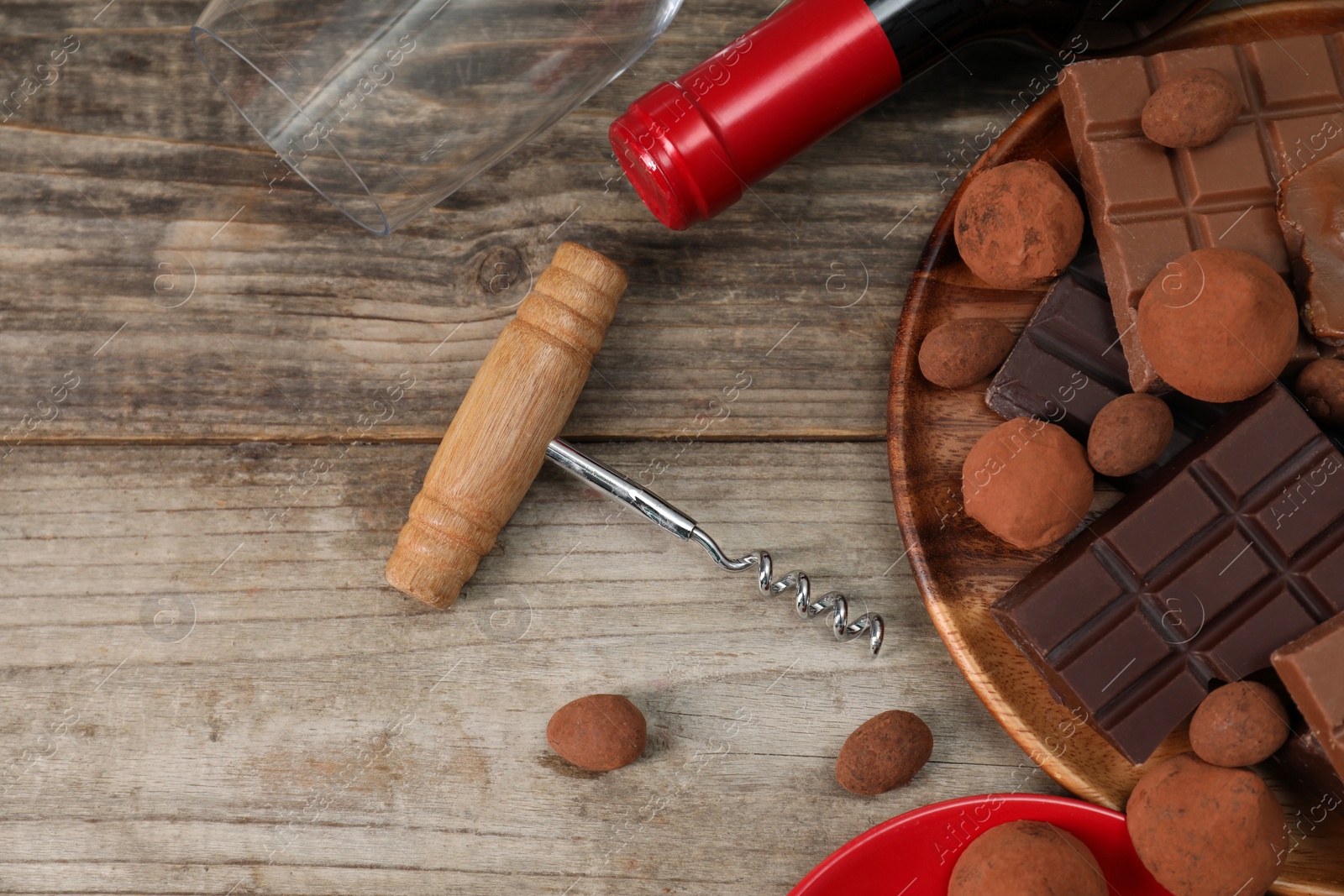 Photo of Bottle of red wine, glass, chocolate sweets and corkscrew on wooden table, flat lay. Space for text