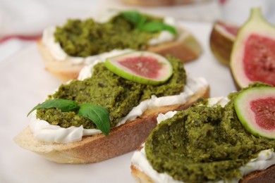 Photo of Tasty bruschettas with cream cheese, pesto sauce, figs and fresh basil on plate, closeup