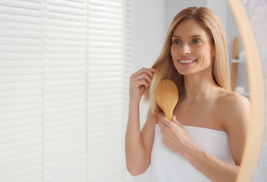 Beautiful woman brushing her hair near mirror in bathroom, space for text