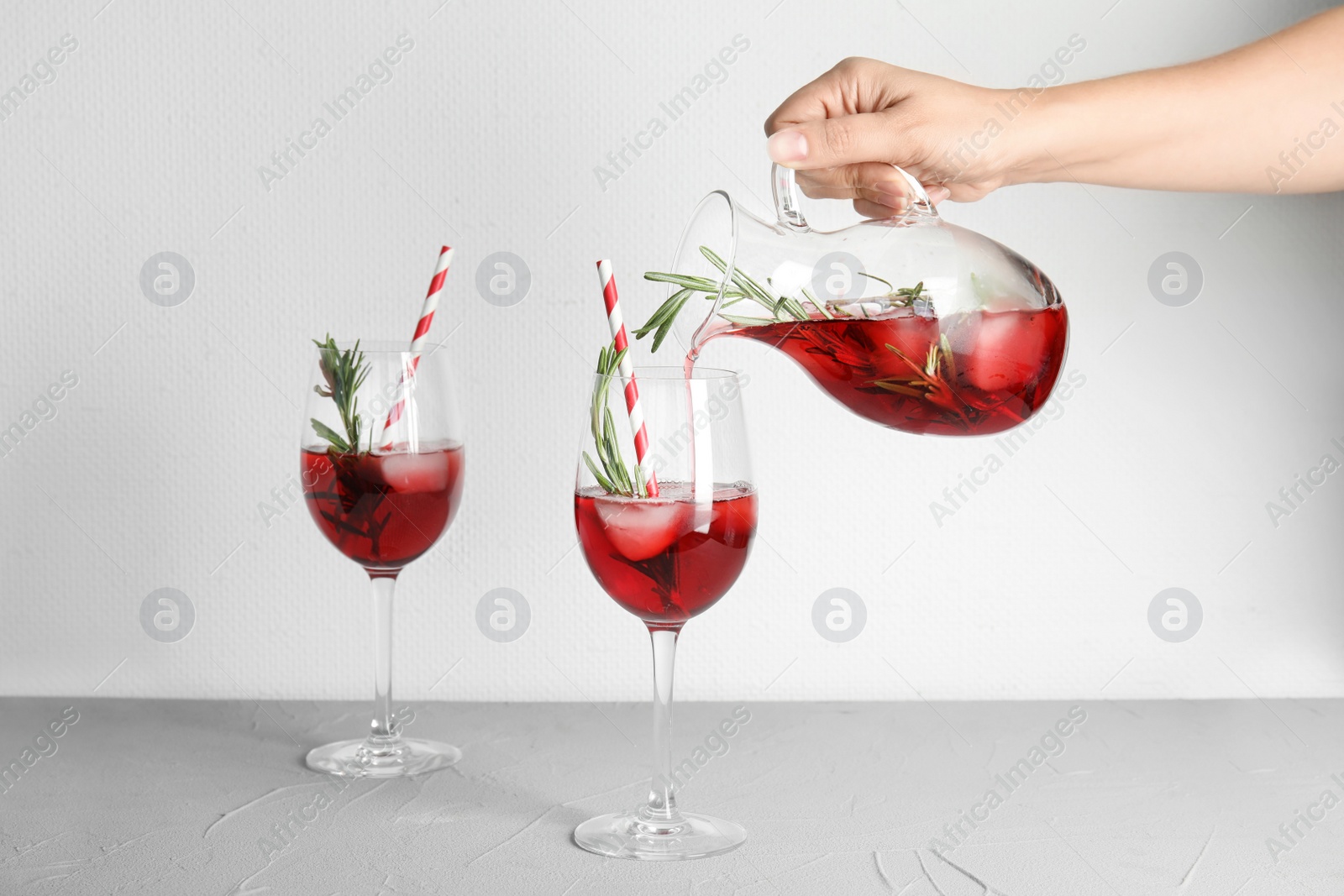 Photo of Woman pouring cranberry cocktail into glass with rosemary on table