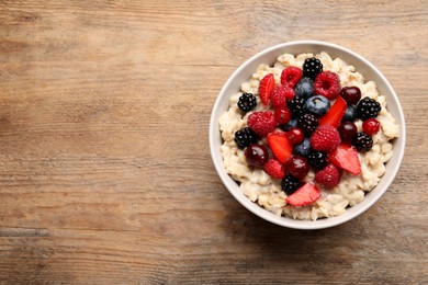 Photo of Bowl with tasty oatmeal porridge and berries on wooden table, top view. Space for text