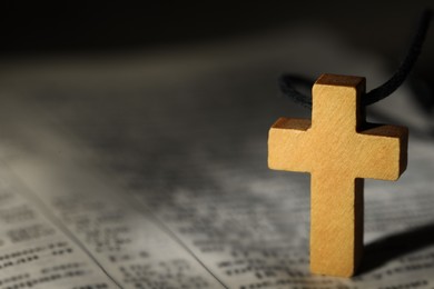 Photo of Wooden Christian cross on Bible, closeup. Space for text