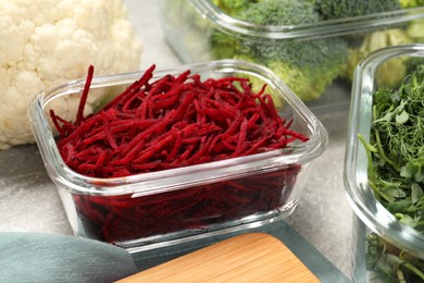 Photo of Glass containers with cut beetroot and fresh products on light gray table, closeup. Food storage