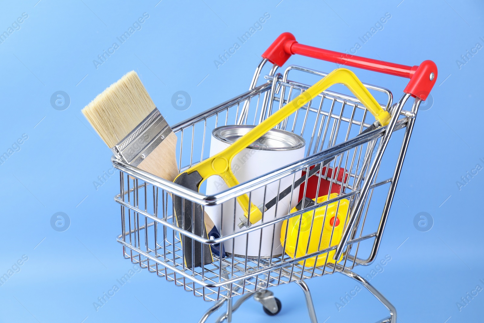 Photo of Small shopping cart with paint and renovation equipment on light blue background