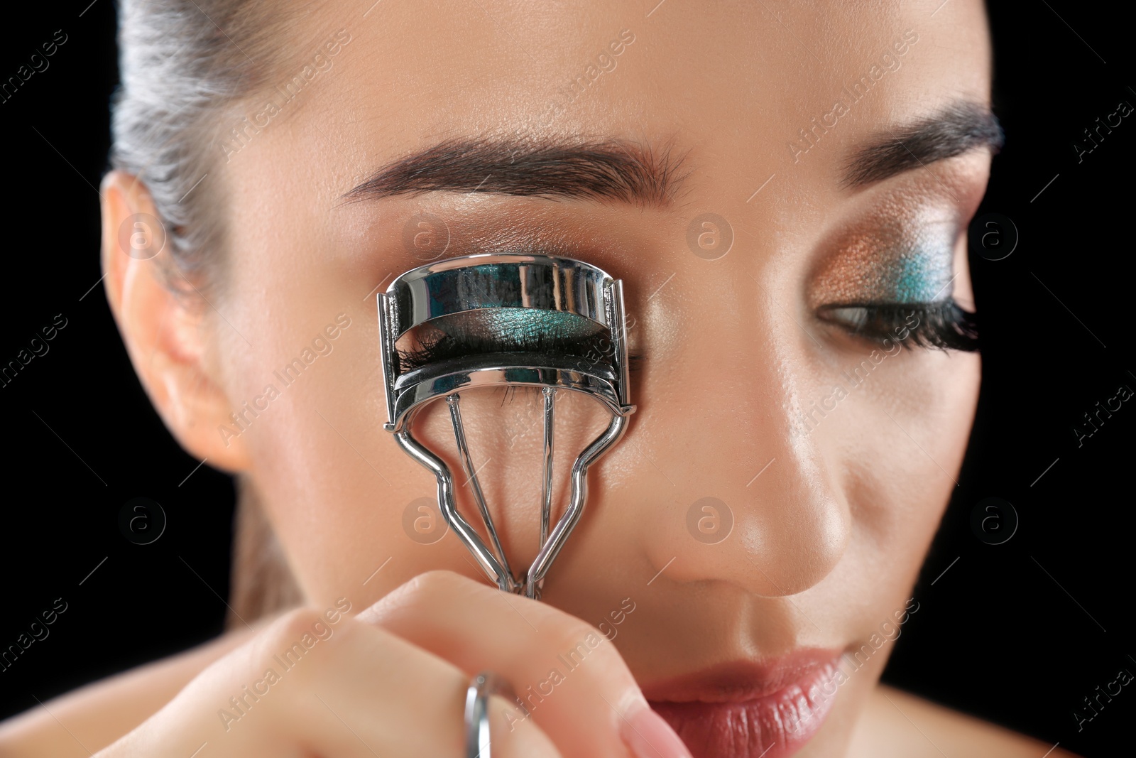 Photo of Young woman curling her eyelash extensions, closeup