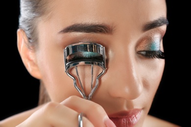 Photo of Young woman curling her eyelash extensions, closeup