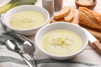 Photo of Bowls of tasty leek soup on white wooden table, closeup