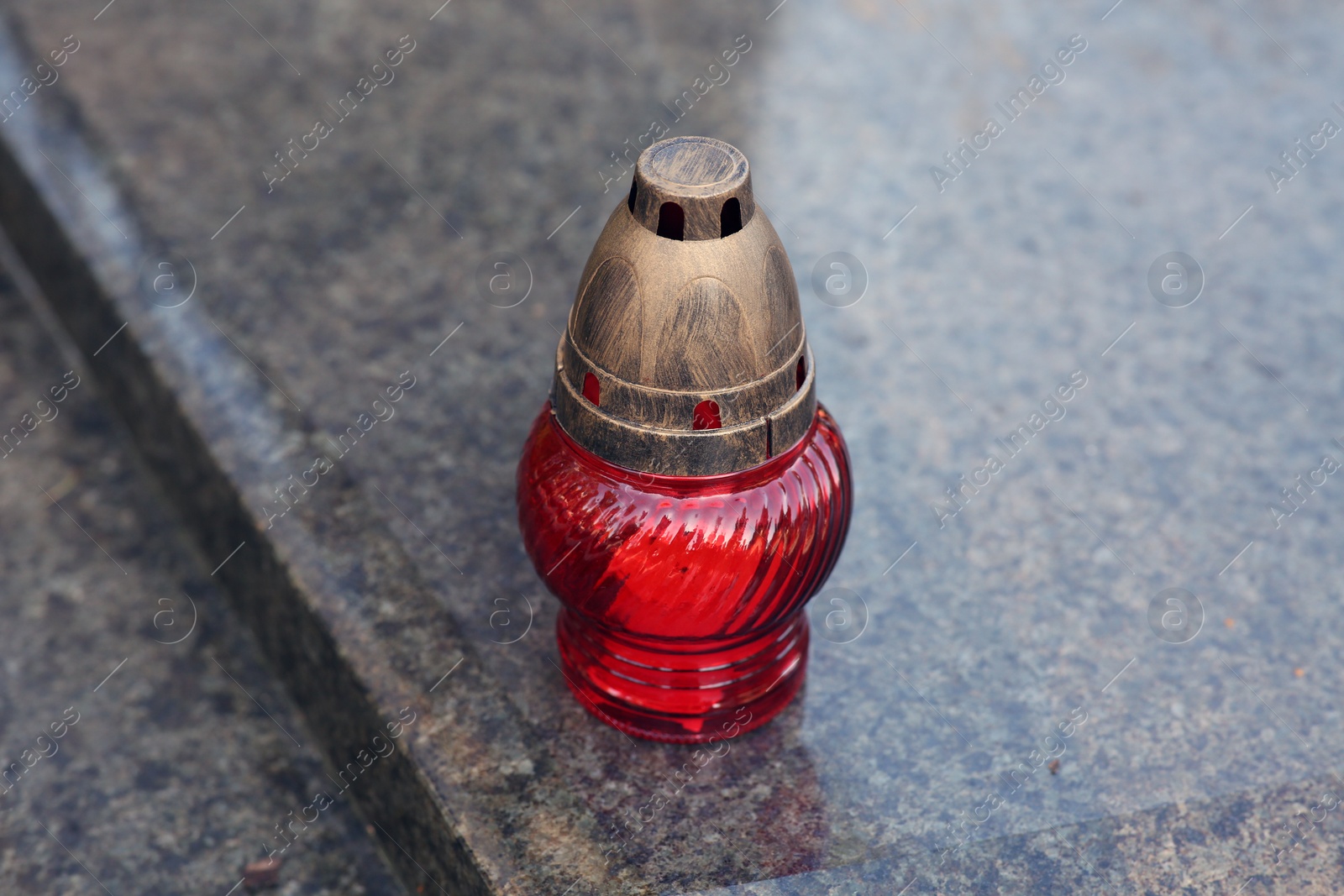 Photo of Red grave lantern with burning candle on granite surface in cemetery