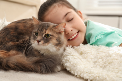 Cute little girl with cat lying on carpet at home. First pet