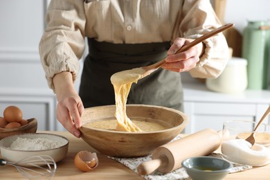 Woman kneading dough with spoon in bowl at wooden table in kitchen, closeup