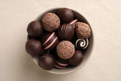 Photo of Many different delicious chocolate truffles in bowl on white fabric, top view