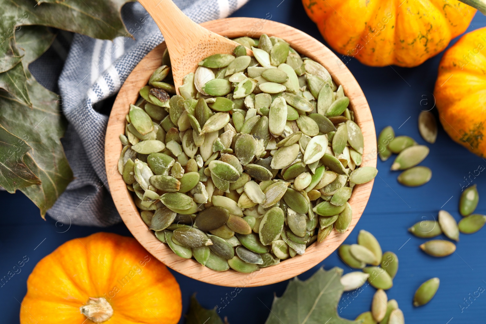 Photo of Bowl with seeds, fresh pumpkins and dry leaves on blue wooden table, flat lay