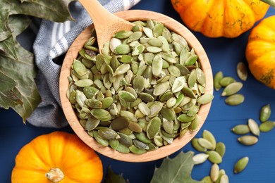 Bowl with seeds, fresh pumpkins and dry leaves on blue wooden table, flat lay