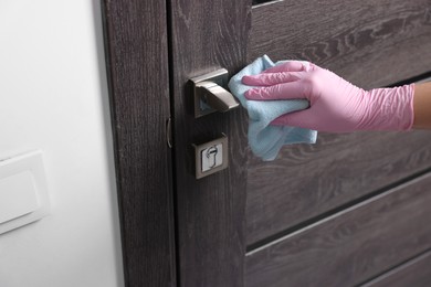 Photo of Woman wiping door handle with rag indoors, closeup