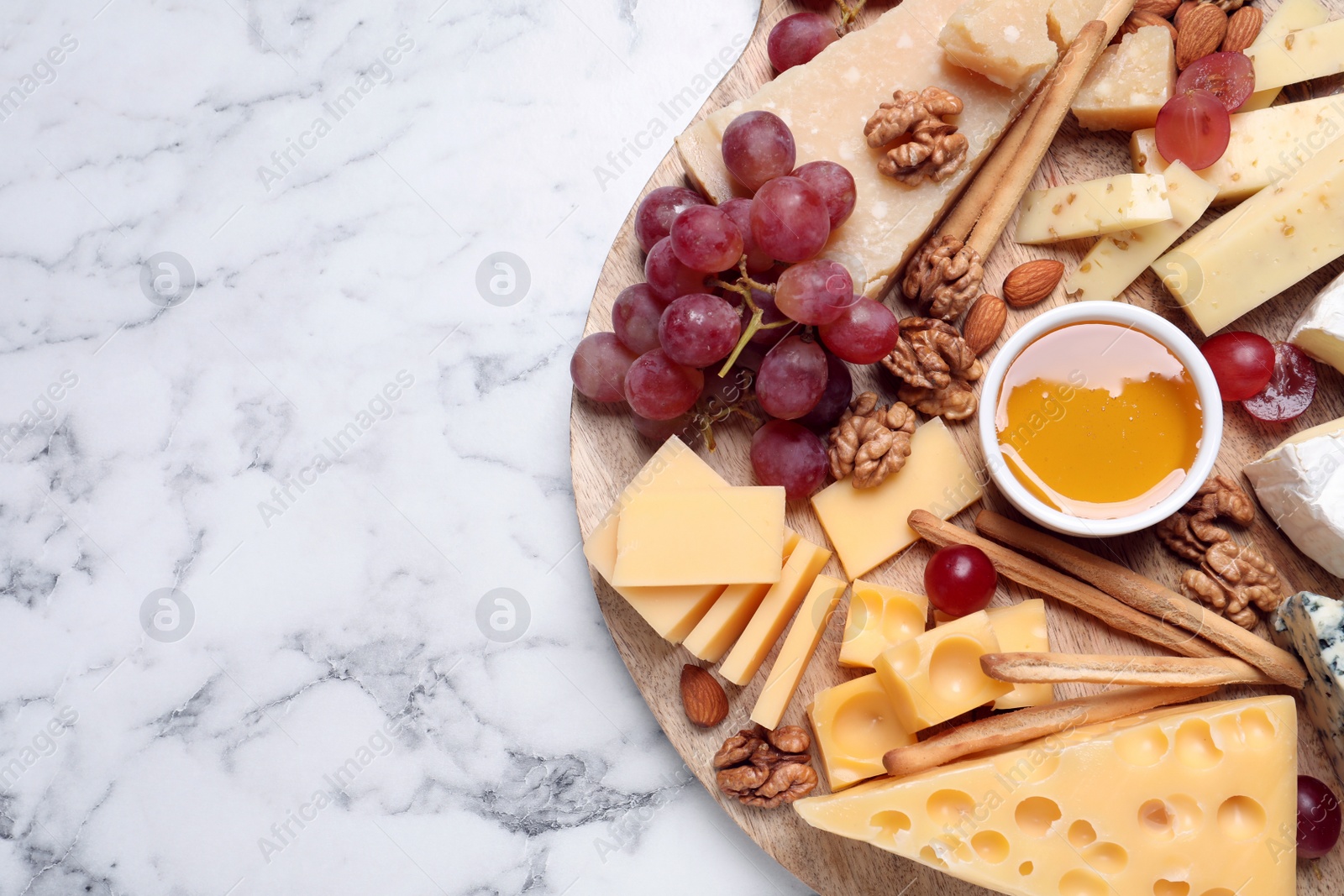 Photo of Cheese plate with honey, grapes and nuts on white marble table, top view. Space for text