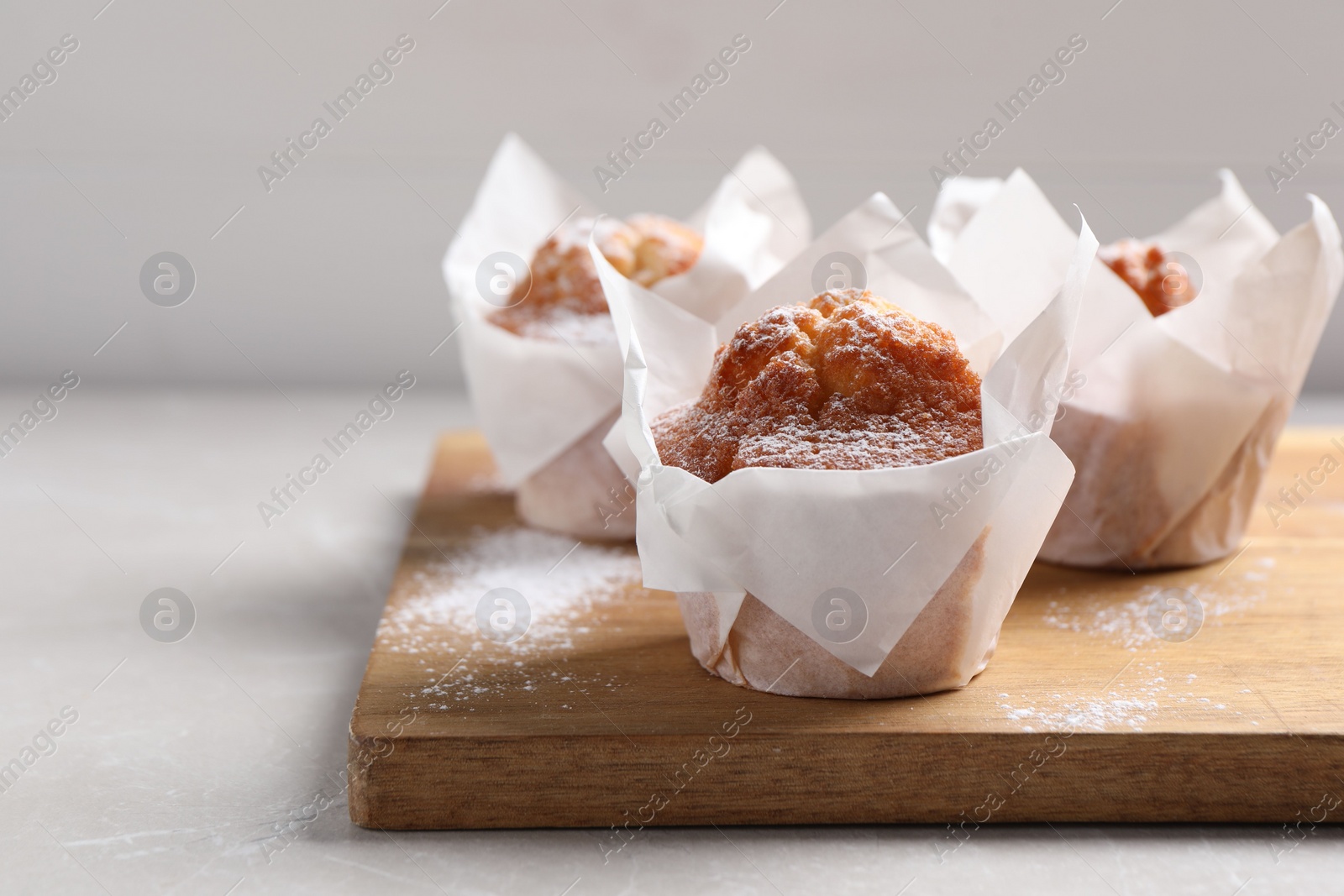 Photo of Delicious muffins with powdered sugar on light table, closeup