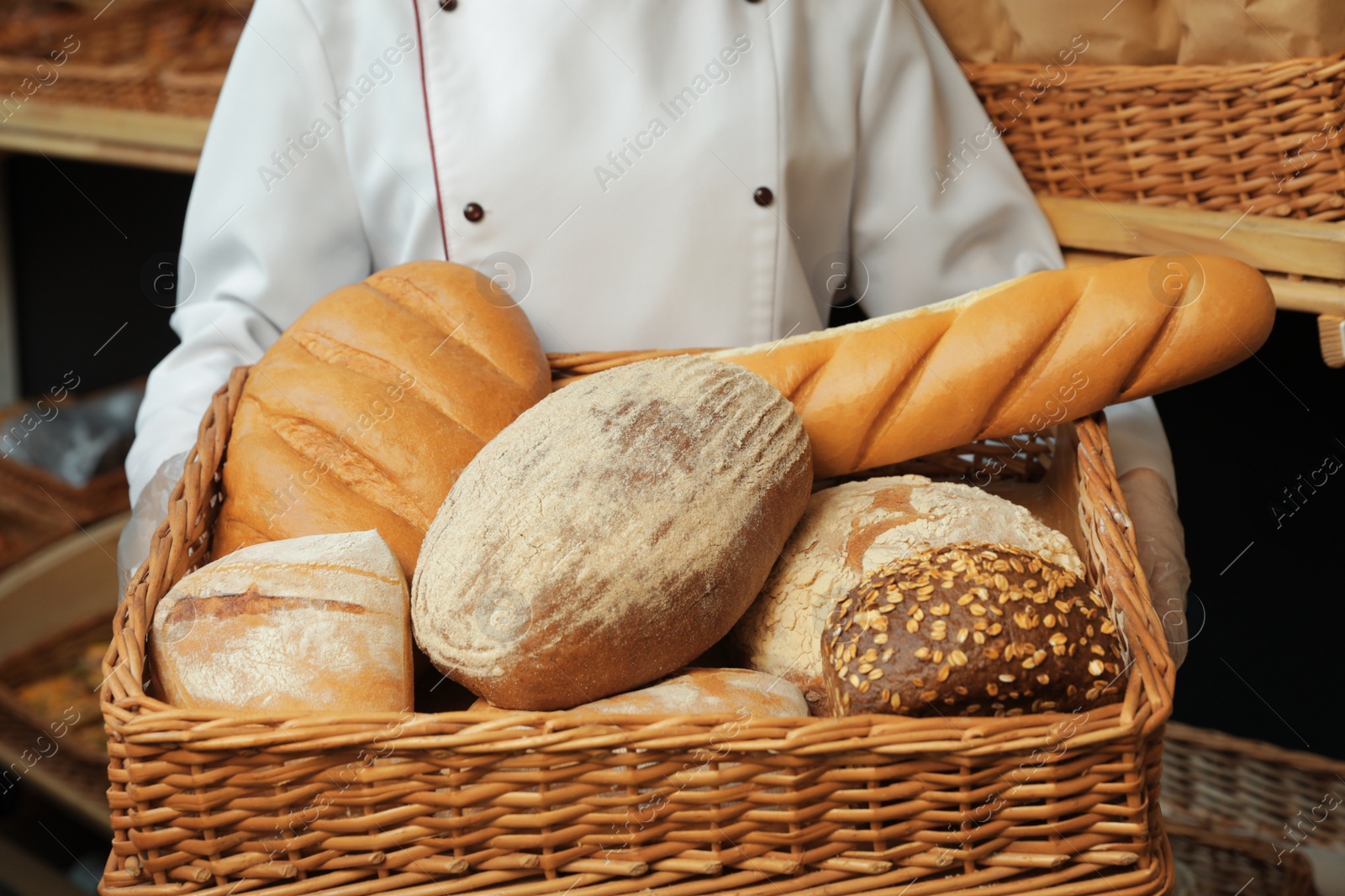 Photo of Professional baker with tray full of fresh breads in store, closeup