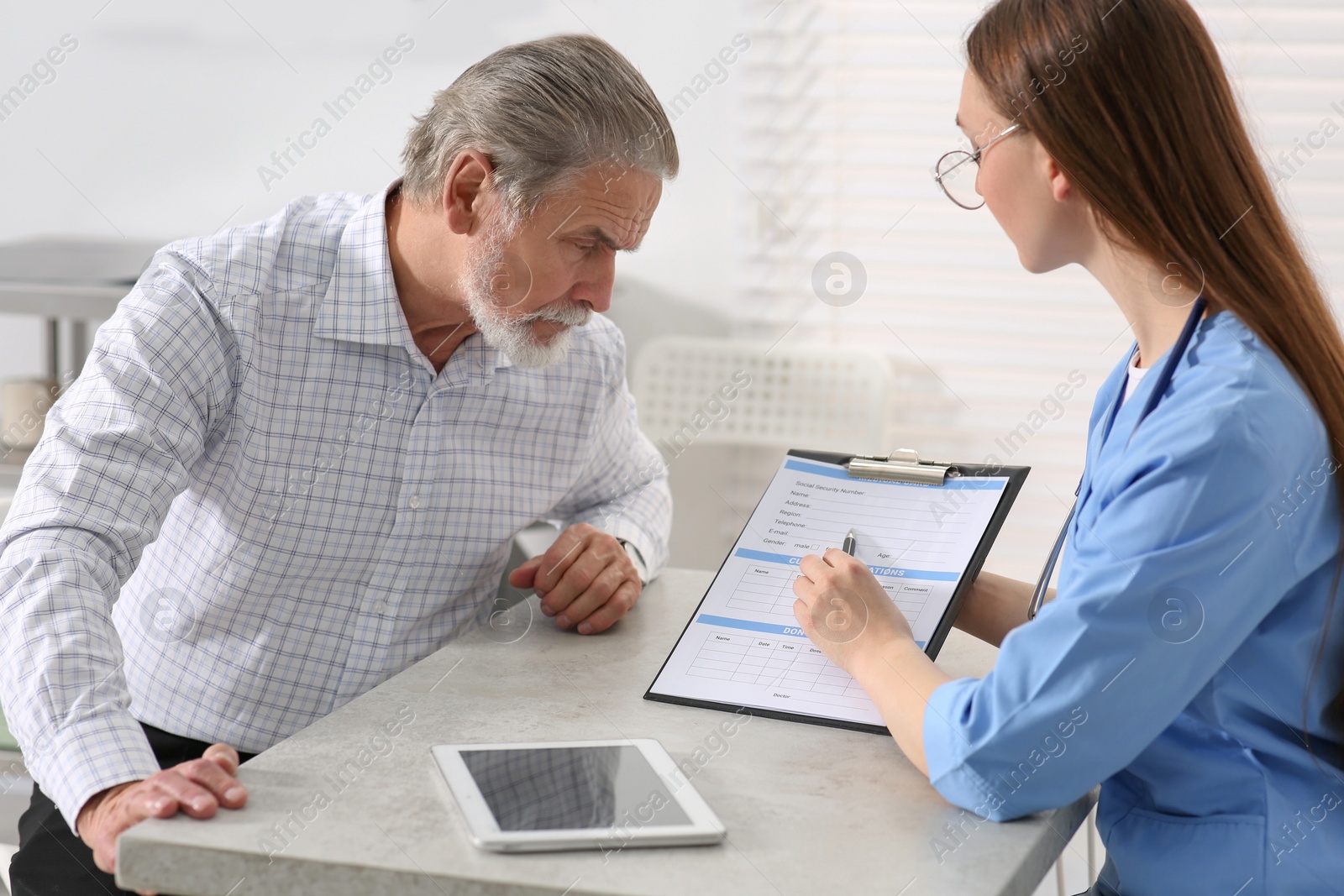 Photo of Doctor showing medical card to patient at table in clinic