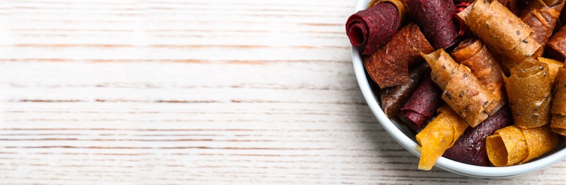 Photo of Delicious fruit leather rolls on white wooden table, top view. Space for text