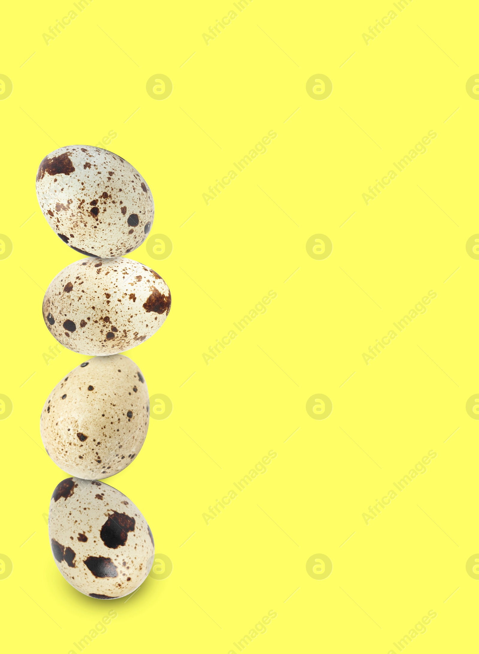 Image of Stacked speckled quail eggs on light yellow background. Space for text