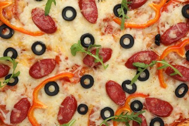 Photo of Tasty pizza with cheese, dry smoked sausages, olives, pepper and arugula as background, top view