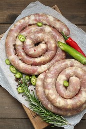 Board with homemade sausages, rosemary, chili and spices on wooden table, top view