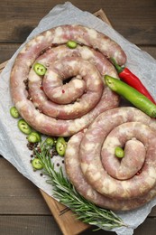 Photo of Board with homemade sausages, rosemary, chili and spices on wooden table, top view