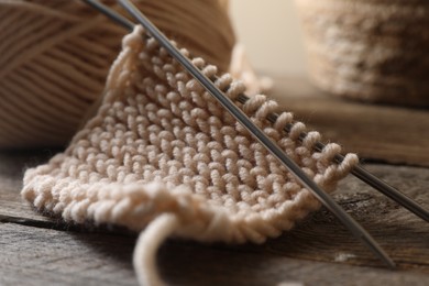 Photo of Soft beige knitting and metal needles on wooden table, closeup