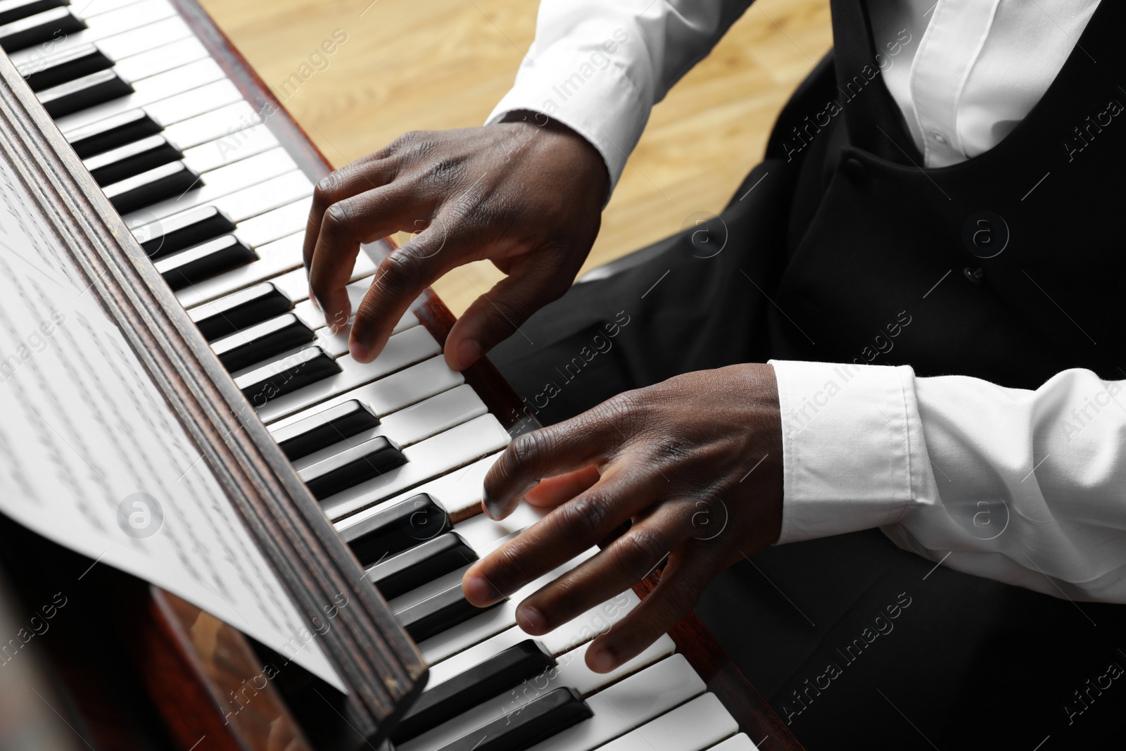 Photo of African-American man playing piano indoors, closeup. Talented musician