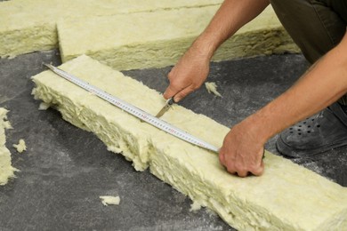 Photo of Worker measuring and cutting insulation material indoors, closeup
