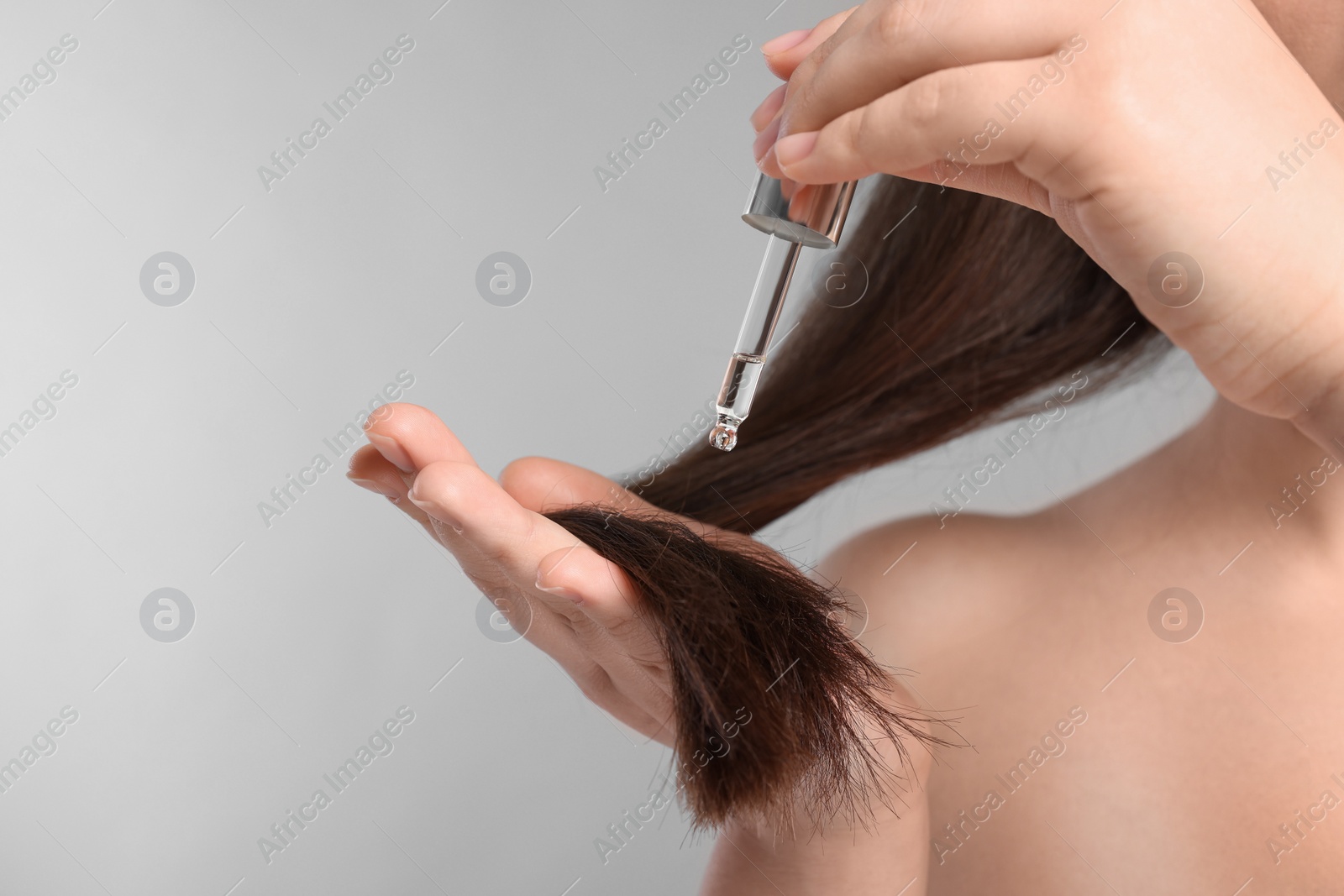 Photo of Woman applying essential oil onto hair on light grey background, closeup