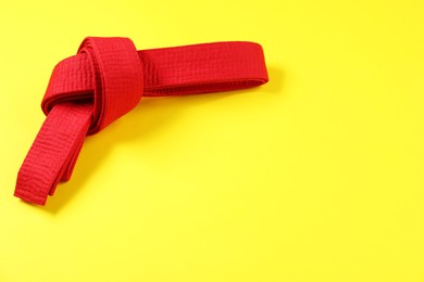 Photo of Red karate belt on yellow background, top view. Space for text